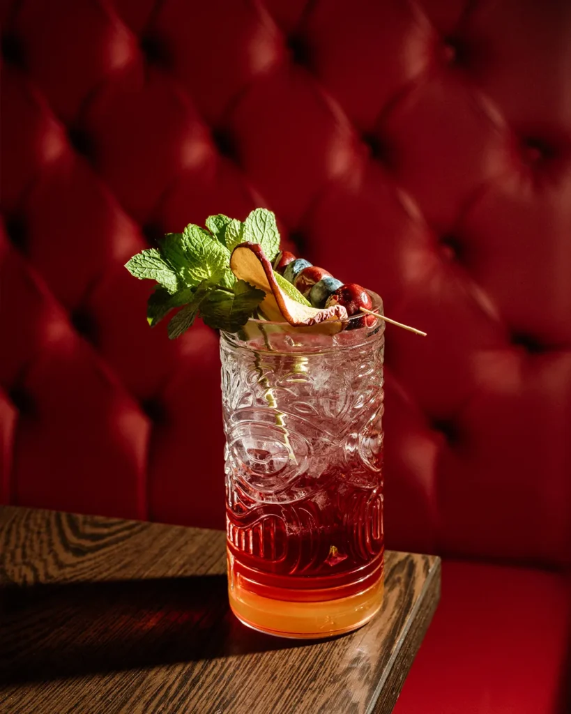 Red cocktail with garnish placed against a red tufted booth, warm evening bar mood