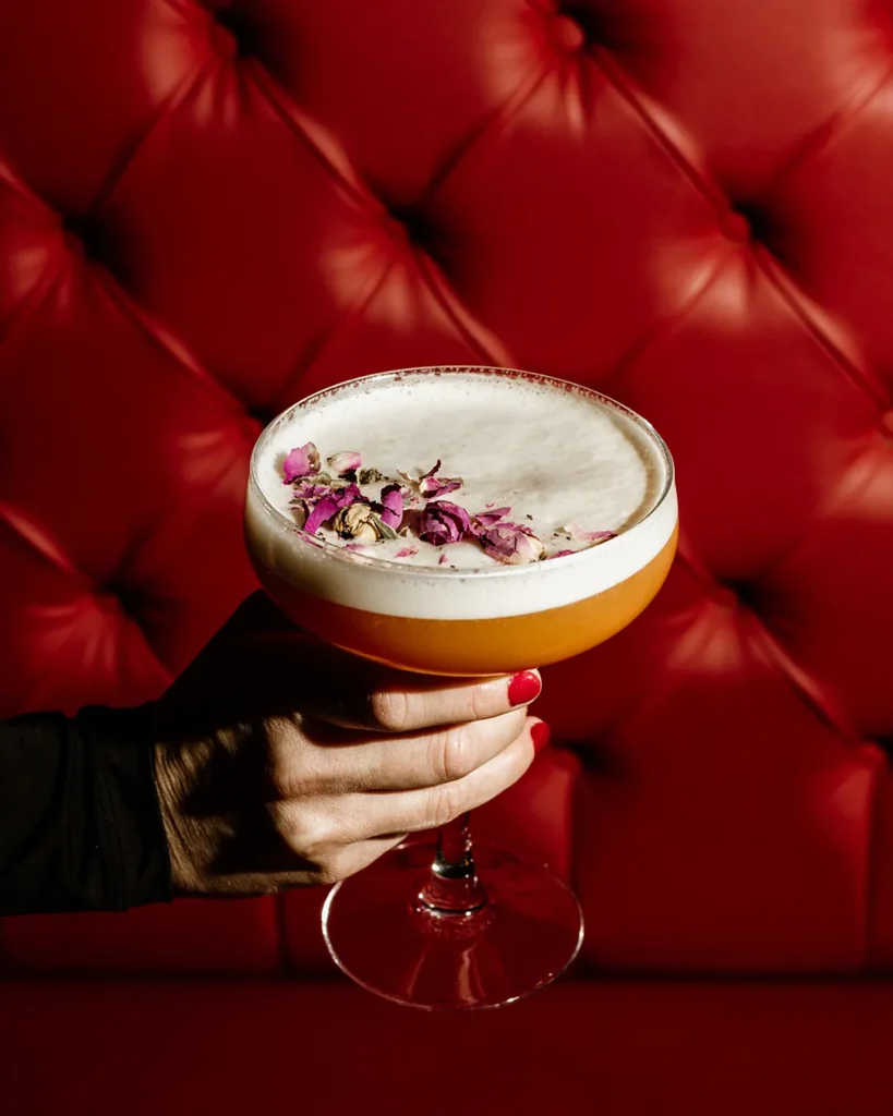 Hand holding a cocktail glass in front of a red tufted booth, intimate lounge atmosphere