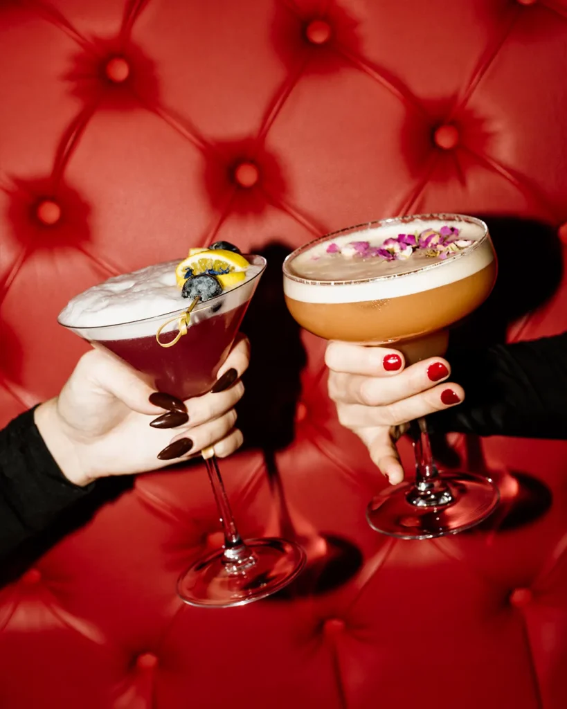 Two cocktail glasses held up together in front of a red tufted booth, cheers moment