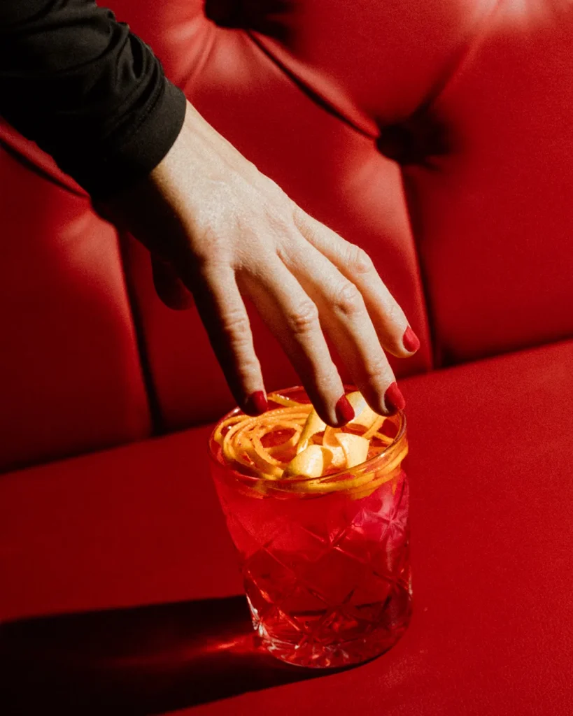 Hand placing an orange-toned drink on a table with a red tufted booth background
