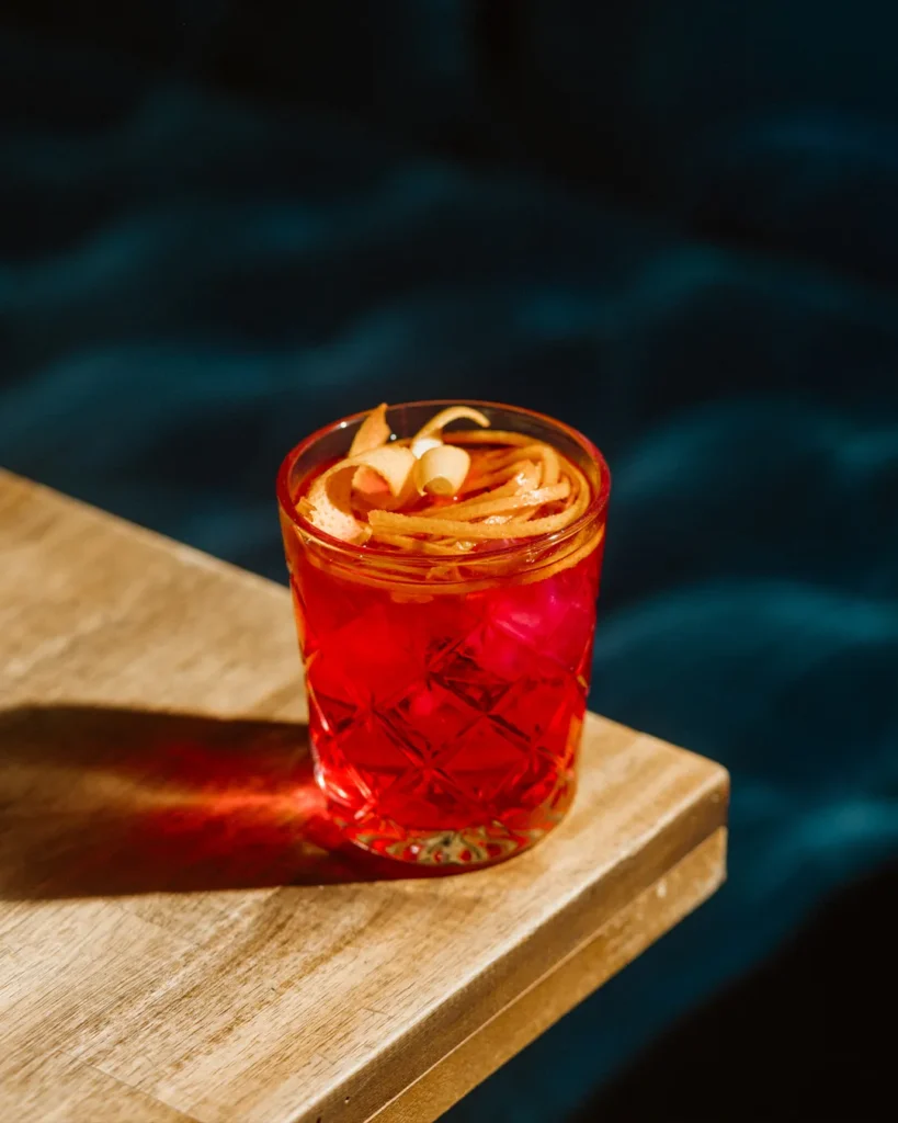 Orange cocktail on a wooden tray with a dark blue booth background, elegant bar styling