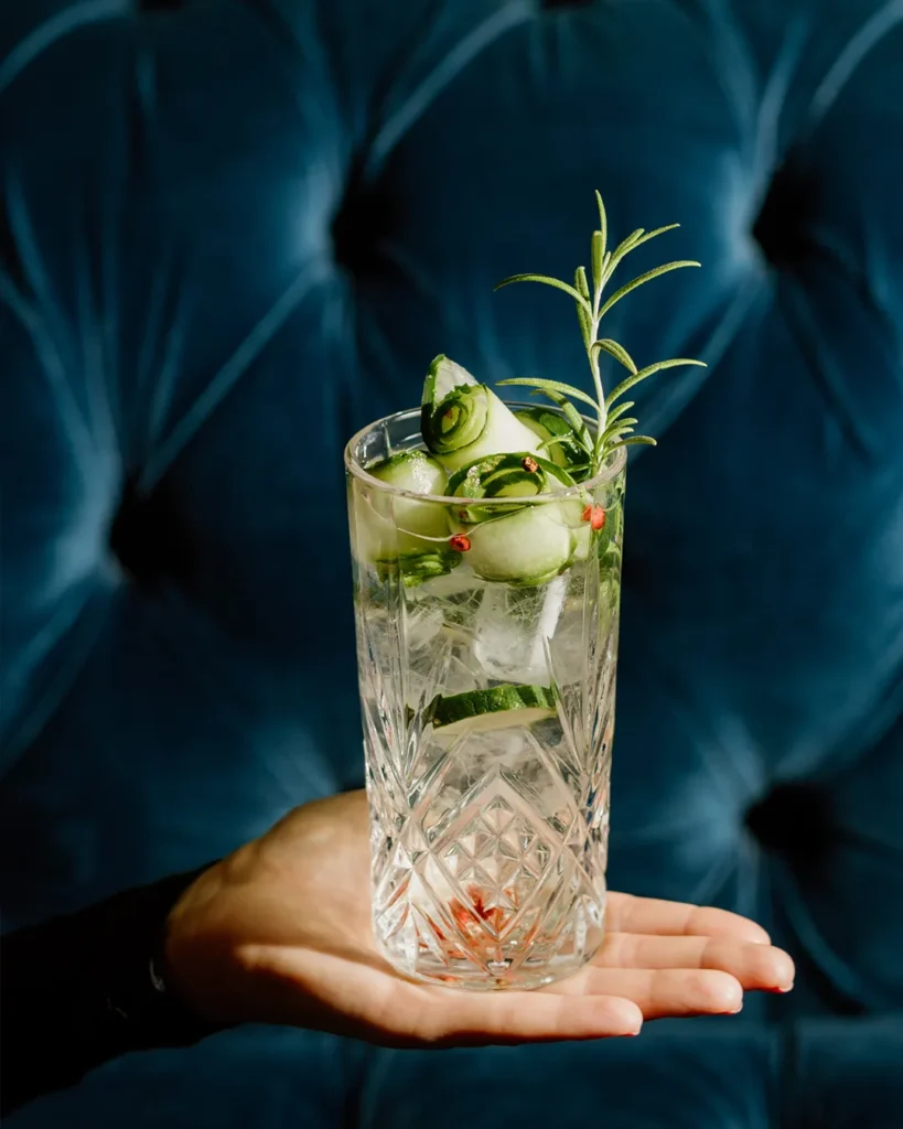 Tall clear cocktail with mint and ice on a wooden table, dark blue booth background