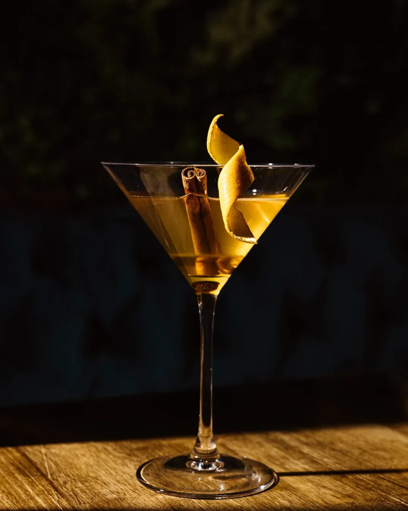 Golden cocktail served in a stemmed glass on a wooden table, dark lounge backdrop