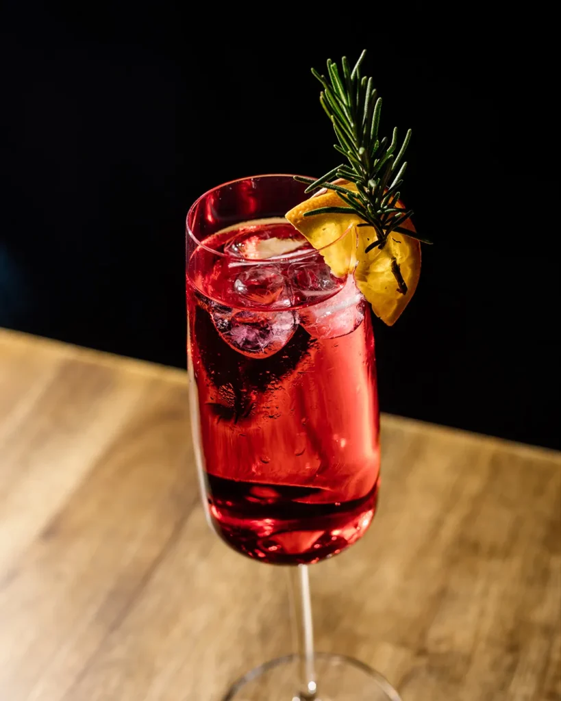 Red long drink with garnish on a wooden table, cinematic bar lighting