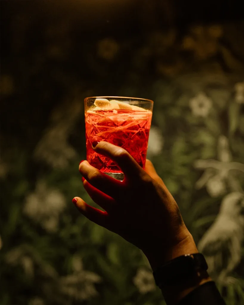 Hand holding a red drink in moody lighting, brand atmosphere and nightlife energy