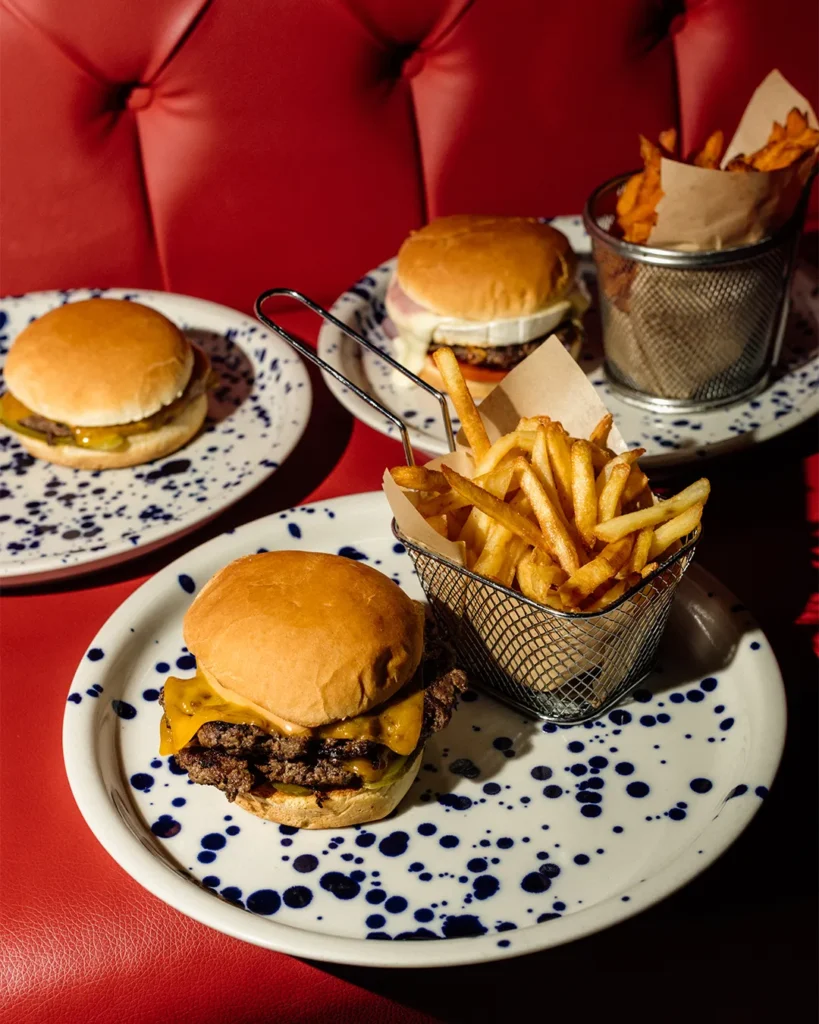 Three burgers served with fries in baskets on a red booth table setting at Escobar Balna