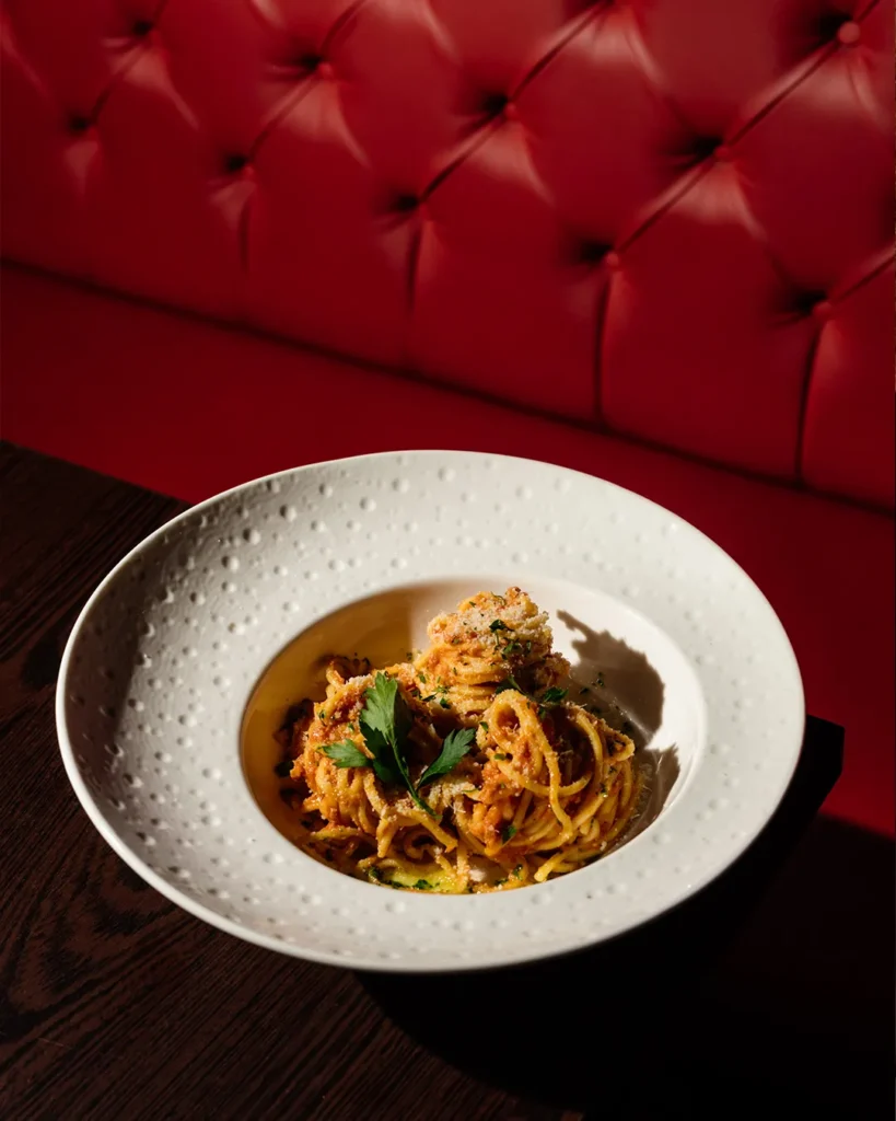 Plated pasta dish on a table with red booth background, premium dining mood