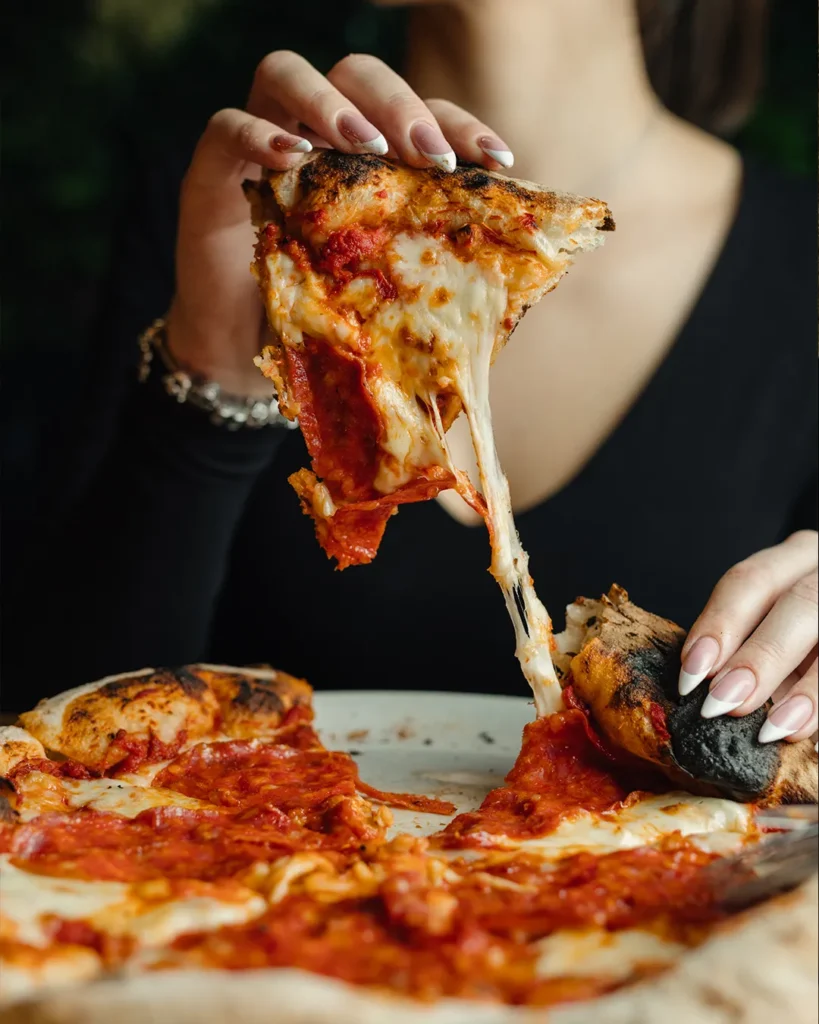 Pizza slice being lifted from a whole pizza, stretchy cheese and toppings visible