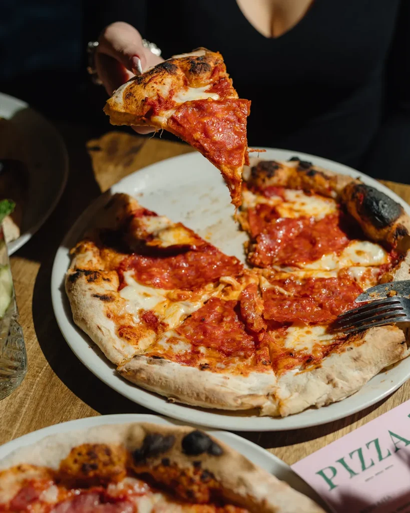 Hands serving pizza slices over a pizza, lively sharing moment at the table