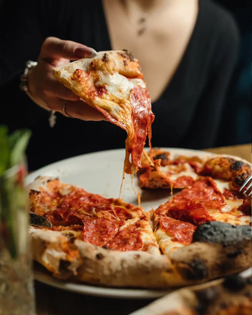 Pizza slice lifted in front of a red tufted booth, bold and cinematic composition