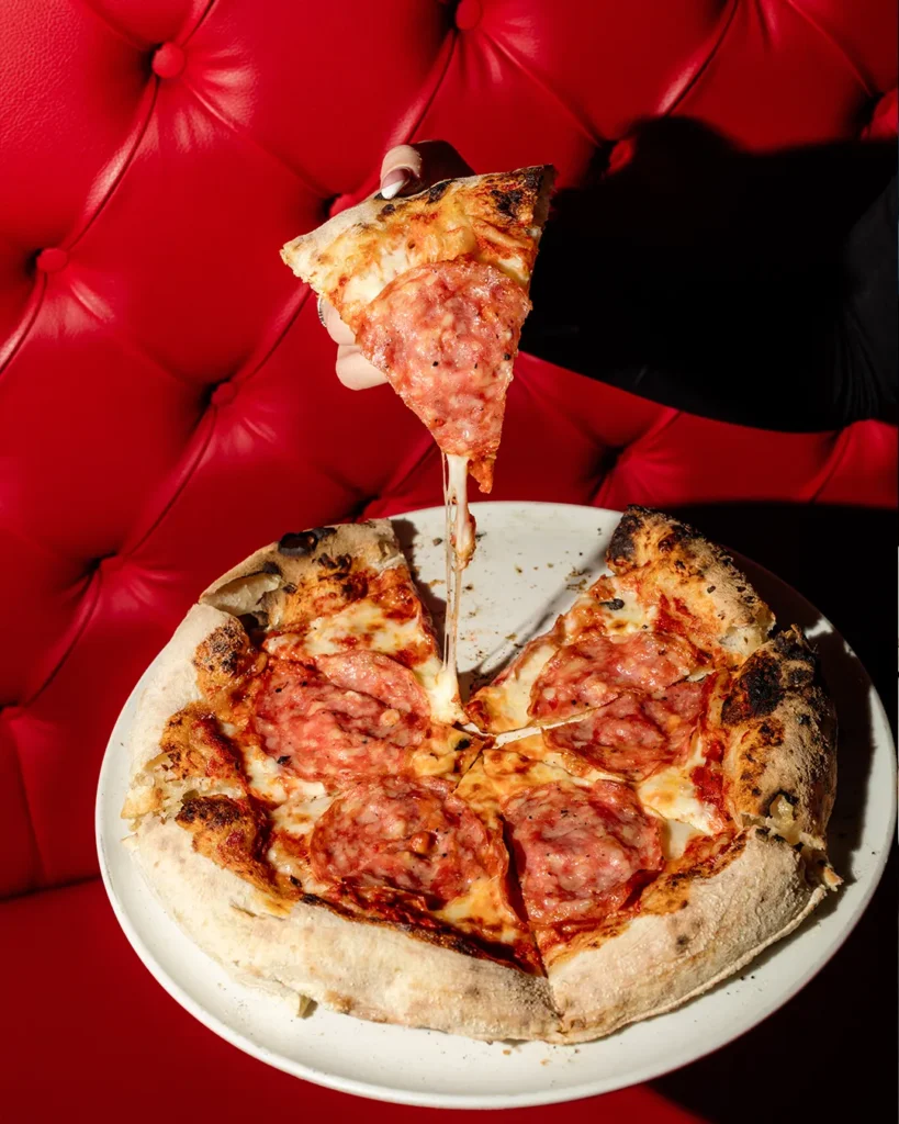Pizza slice being lifted from a pizza with red booth backdrop, strong menu-style visual