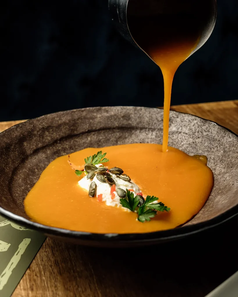 Golden soup or sauce being poured into a bowl, close-up action shot with rich texture