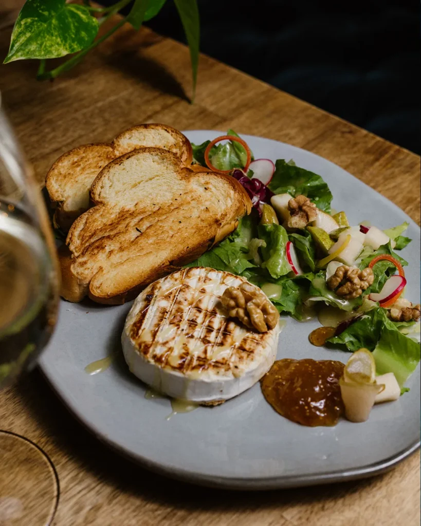 Plated sharing dish with bread and greens, bright natural table lighting